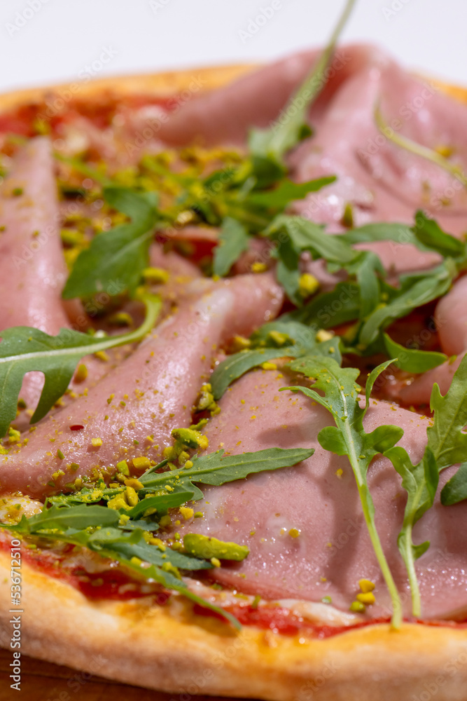 Pizza with ham, arugula and pistachios served on wooden platter Pizza with ham, arugula and pistachios served on wooden platter