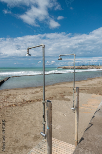 On a deserted sandy beach there are two ageing showers waiting for bathers.