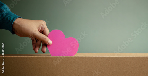 Donation Concept. Hand Droping a Pink Paper Heart into a Donate Box. Helping, Supporting and Togetherness. Side View photo