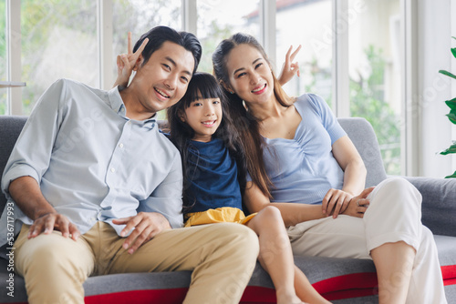 Cheerful young family father mother and daughter smiling embrace sitting on couch in living room at home, Family quality time concept