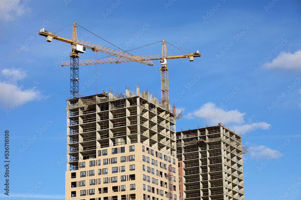 Tower cranes and unfinished buildings on background of blue sky with white clouds. Housing construction, apartment blocks in city