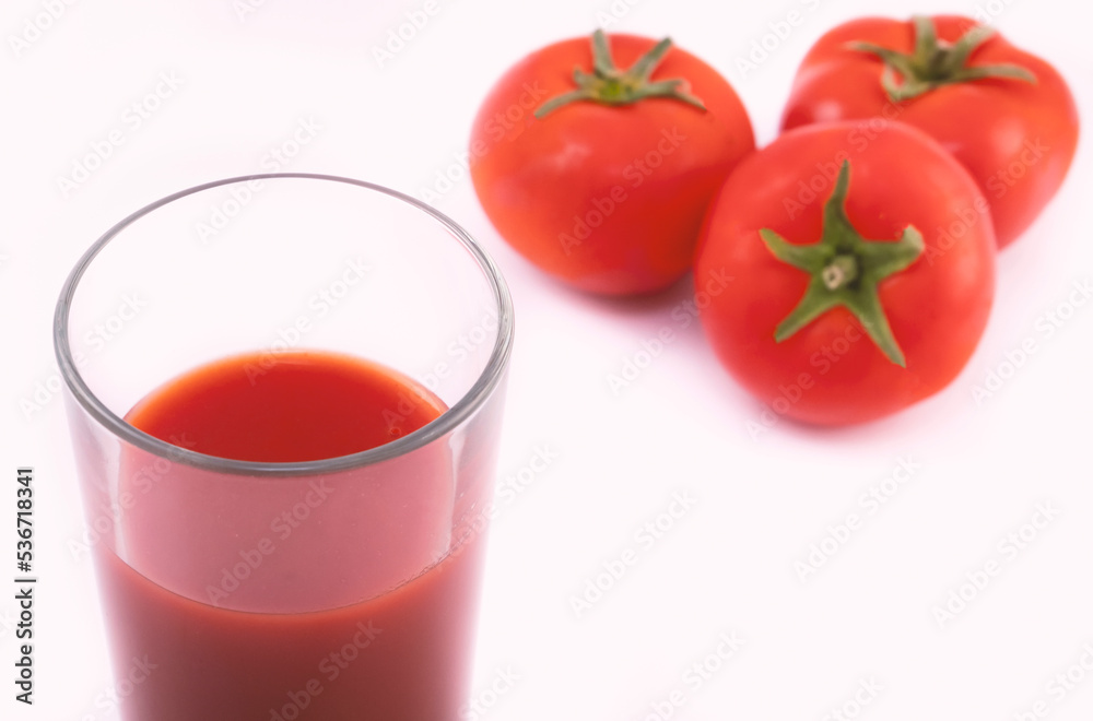 Tomato juice in a glass and ripe tomatoes on a white background