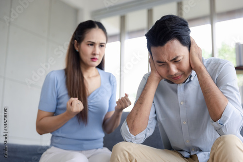Unhappy asian couple quarreling sitting on couch at home, Frustrate mad young wife shouting man husband closing ears. Family conflict break up or divorce concept