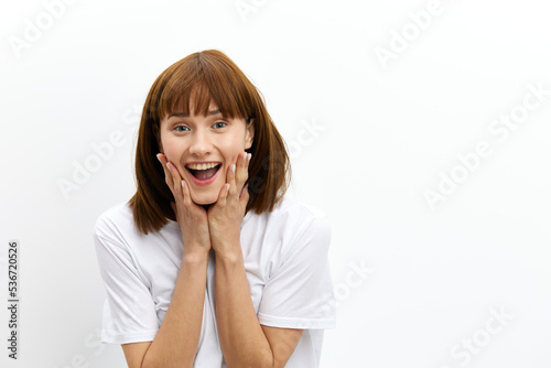 a happy, joyful woman smiles pleasantly with beautiful, even teeth and holds her hands near her face standing on a white background in a white T-shirt