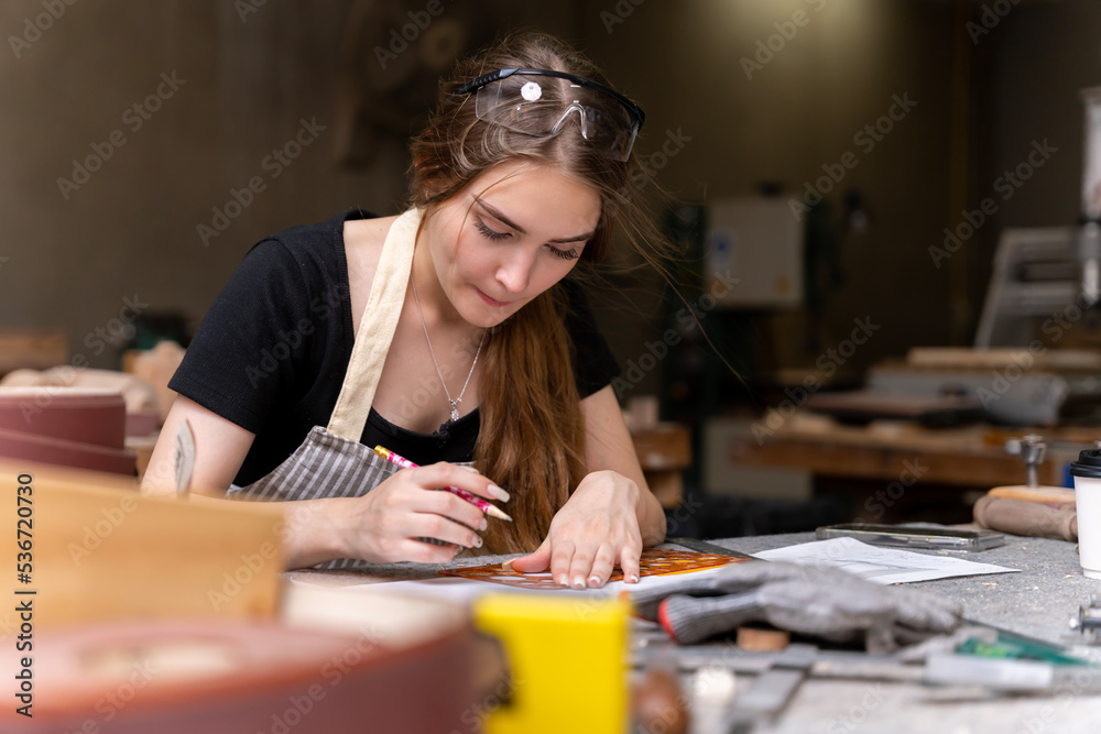 Portrait of a female carpenter drawing on paper for designing and building furniture in a furniture factory. with modern tools Portrait of a female carpenter drawing on paper for designing and building furniture in a furniture factory. with modern tools