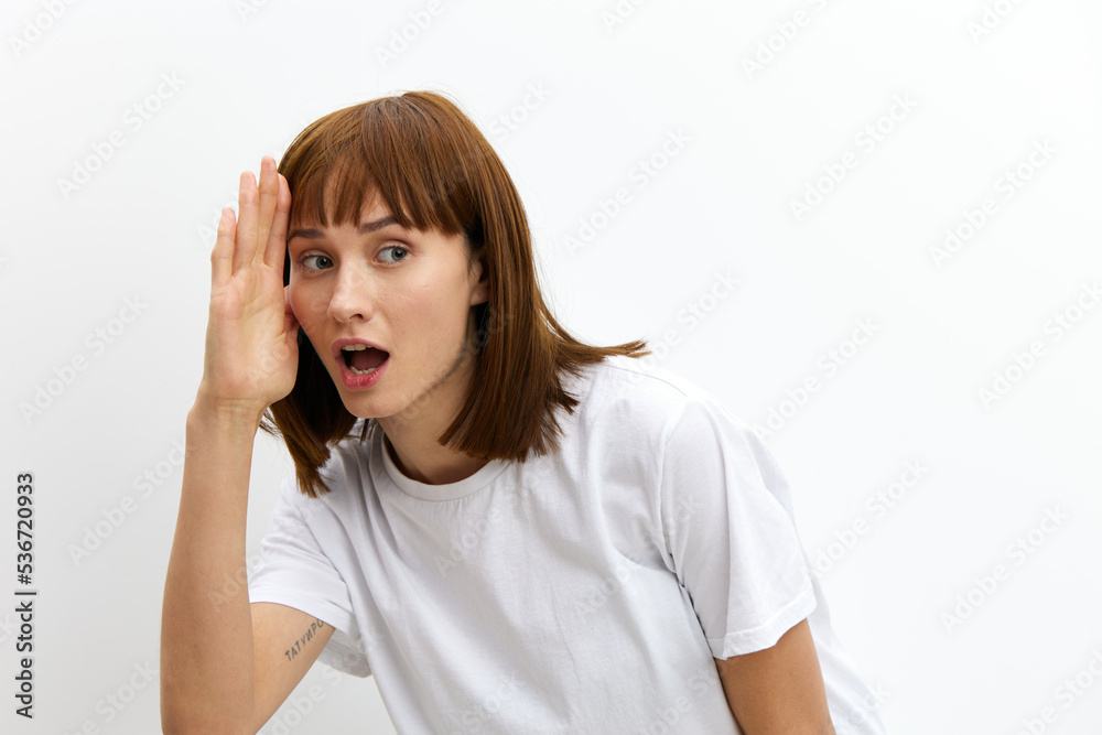 a funny, funny, cheerful woman stands on a white background in a white T-shirt and leaning her hand to her forehead looks at the camera smiling sweetly a funny, funny, cheerful woman stands on a white background in a white T-shirt and leaning her hand to her forehead looks at the camera smiling sweetly
