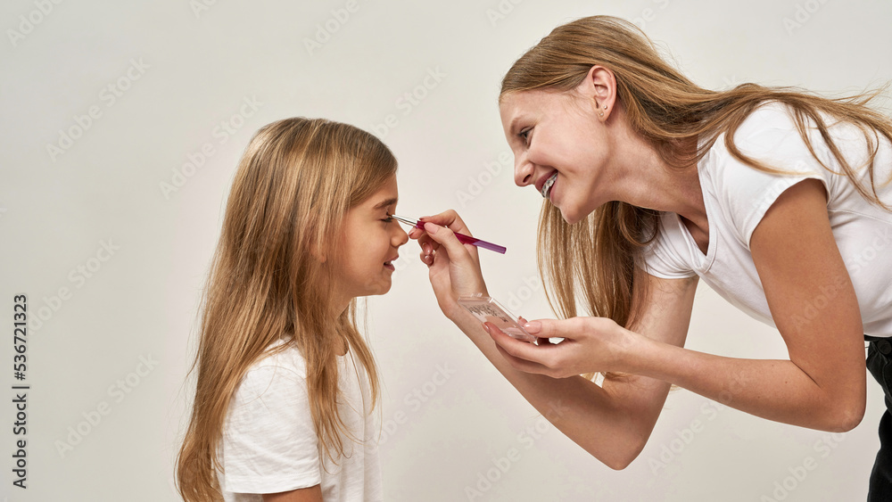 Side of girl painting glitter eyelid of sister