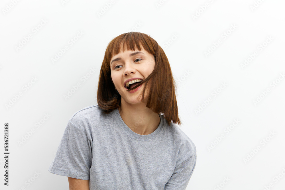 a beautiful, happy woman stands on a white background in light clothes with straight, red hair and looks away smiling broadly