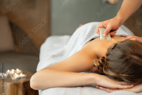 Gouache massage. The girl lies on the massage table, the man's hand makes a massage with a stone in the office with candles. photo