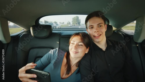 A young couple rides in the back seat of a taxi, they talk, smile, laugh, the girl takes a selfie on her phone. A clear sunny day. Slow motion 4k footage