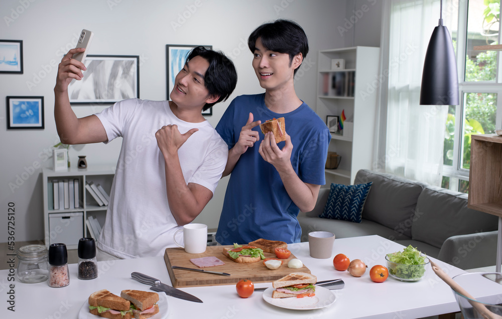 Young Asian gay couple looking happy while cooking and taking selfie. LGBT men couple preparing meal salad in the kitchen at home. Young Asian gay couple looking happy while cooking and taking selfie. LGBT men couple preparing meal salad in the kitchen at home.