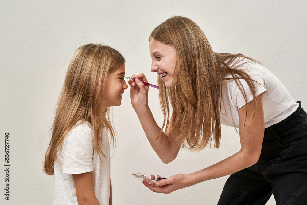 Girl painting glitter eyelid of sister on white Girl painting glitter eyelid of sister on white