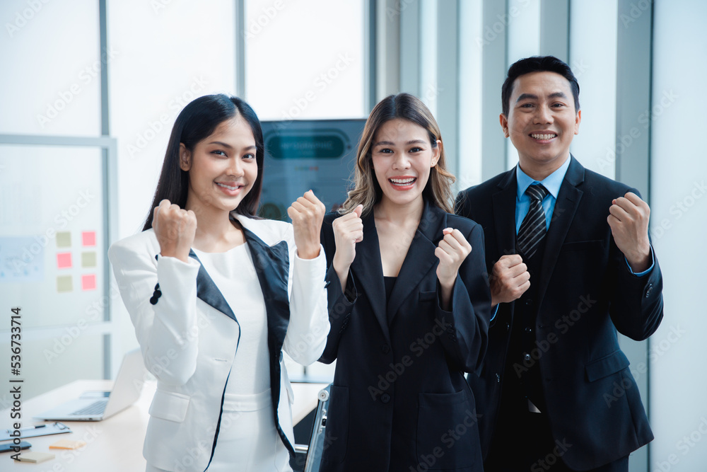 Portrait of asian business group people in suit standing in modern office smiling raising hand celebrating success teamwork Portrait of asian business group people in suit standing in modern office smiling raising hand celebrating success teamwork