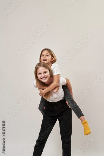 Teenager hold sister piggyback on white background