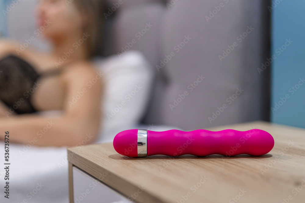 Poster Young woman holding sex toy dildo vibrator in bed  