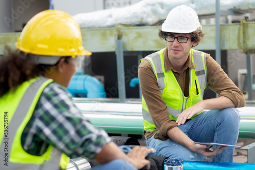 Young woman and man engineer examining pipeline and talking in the factory, mechanic or technician inspector and check plumber valve and discussion together, industrial and maintenance concept.