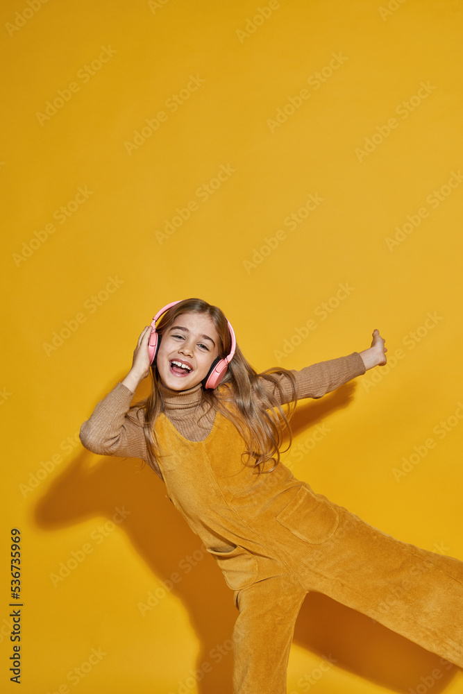 Obraz premium Joyful girl listen music in headphones and dance