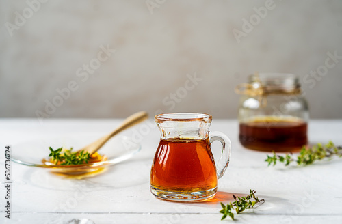 Thyme honey in small jug and jar, small thyme branch on white wooden table with grey background