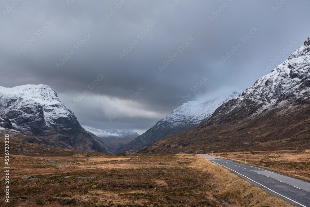 Stunning Winter landscape image of snowcapped Three Sisters mountain range in Glencoe Scottish Highands with dramatic sky