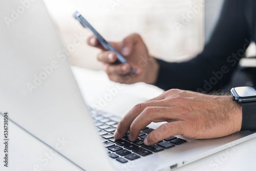 Man types on laptop keyboard and holds mobile phone, close-up photos