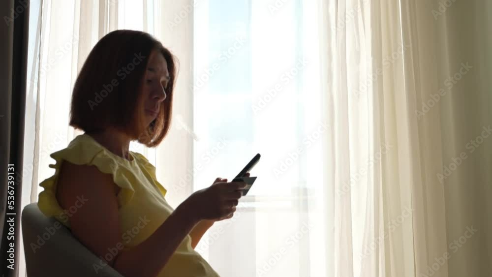 Woman sitting on a chair with smartphone and credit card. Internet purchase concept. 4k footage UHD 3840x2160 Woman sitting on a chair with smartphone and credit card. Internet purchase concept. 4k footage UHD 3840x2160