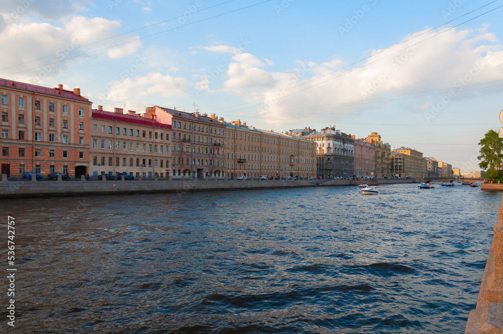 Saint Petersburg, Russia - July 21, 2021: River boats sail along the river channel along the old houses. Summer day, blue sky, clouds