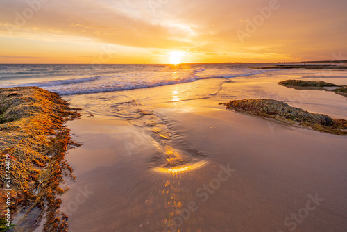 A golden sunset over the ocean reflecting in a wet sandy beach between rocks photo