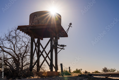 Silhouette of a high tank stand with an old water tank on top and the Sun peaking out from behind