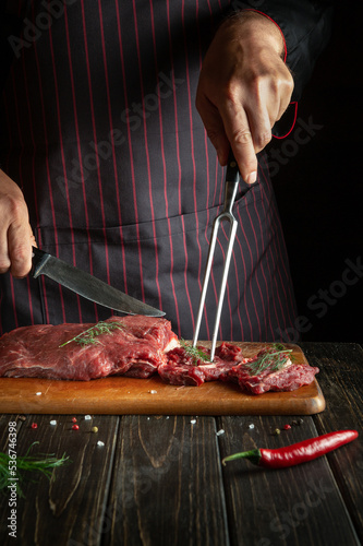 The chef prepares raw fresh beef meat for roasting or barbecue. Working environment in the kitchen of a restaurant or hotel