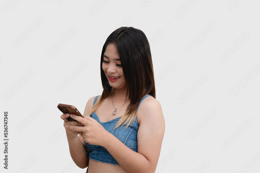 A smiling Asian teenager scrolls through her social media accounts on her cellphone. Isolated on white background studio shot. A smiling Asian teenager scrolls through her social media accounts on her cellphone. Isolated on white background studio shot.