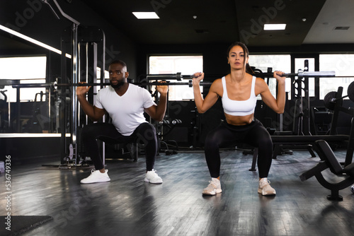 Attractive sports people are working out with barbells at gym.