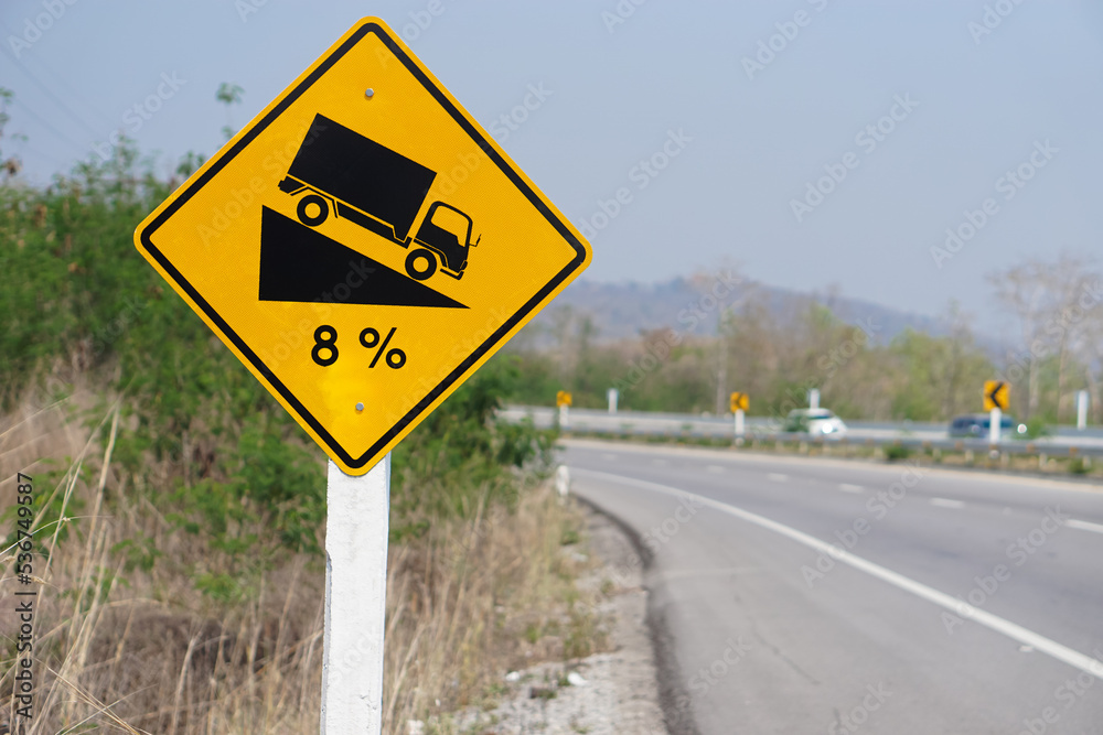 Yellow traffic sign to warn truck driver to drive carefully down to hill on slope a steep 8 percent(8%) downhill gradient beside the road. Concept : Traffic Road Sign and symbol. Yellow traffic sign to warn truck driver to drive carefully down to hill on slope a steep 8 percent(8%) downhill gradient beside the road. Concept : Traffic Road Sign and symbol.