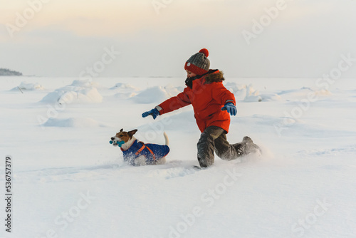 On pleasant winter day kid chasing family pet dog in deep snow