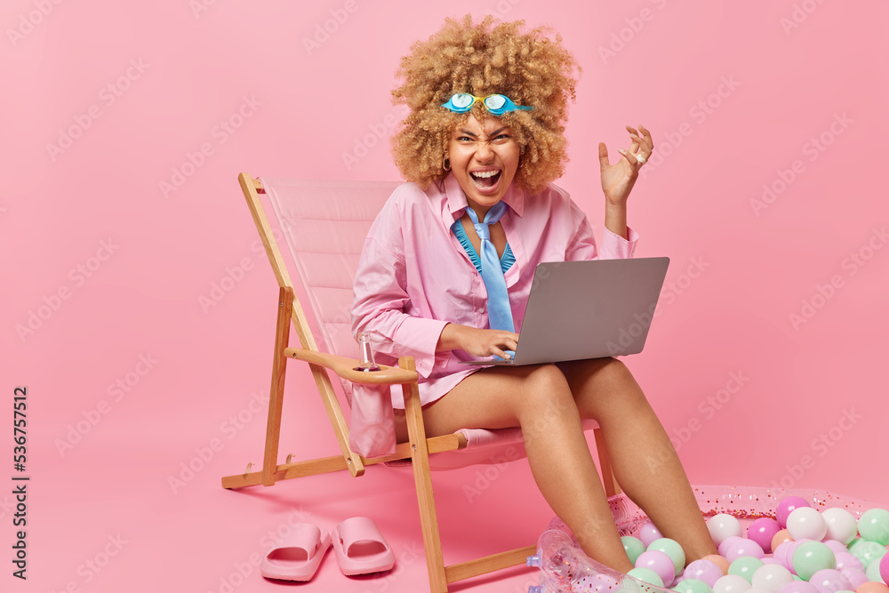 Φωτογραφία Outraged curly haired woman screams angrily works on laptop computer wears swimm