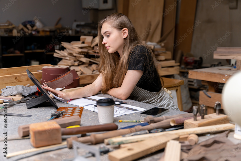 Portrait of a female carpenter looking at designs on a tablet for making her furniture in a furniture factory. with many tools and wood Portrait of a female carpenter looking at designs on a tablet for making her furniture in a furniture factory. with many tools and wood