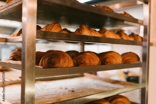 Production of delicious buns. Family bakery. Hot croissants on a metal tray. Fresh bakery. Rack with baked croissants. Beautiful fresh crispy croissants just out of the oven.