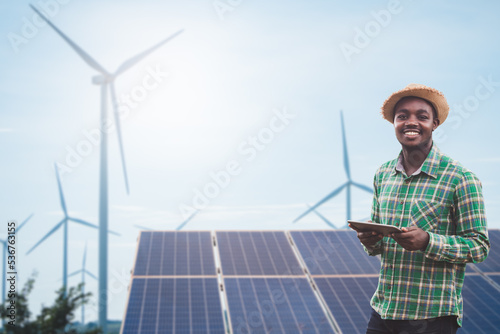 African farmer standing and holding digital tablet on corn farm with solar cell and wind turbine in background.Concept of green power sustainability resources  development by alternative energy. photo