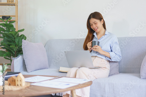 Business at home concept, Businesswoman reading marketing plan data on laptop and drinking coffee