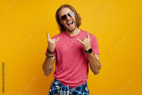 Excited young man gesturing and smiling while standing against yellow background