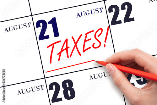Hand drawing red line and writing the text Taxes on calendar date August 21. Remind date of tax payment