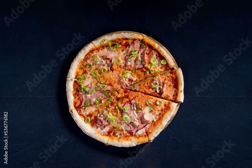 Delicious pizza with mozzarella cheese, ham, leeks on a tomato base on black background
