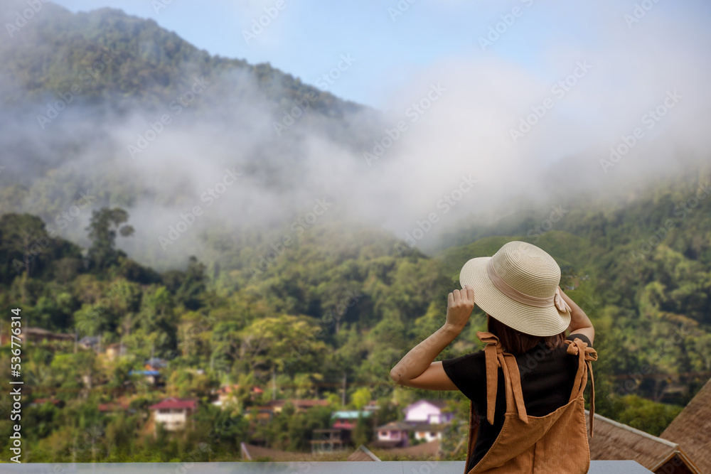 back view of woman wearing black t-shirt and hat lift smart phone up to take a photo,seeing the nature foogy over mountain,travel concept