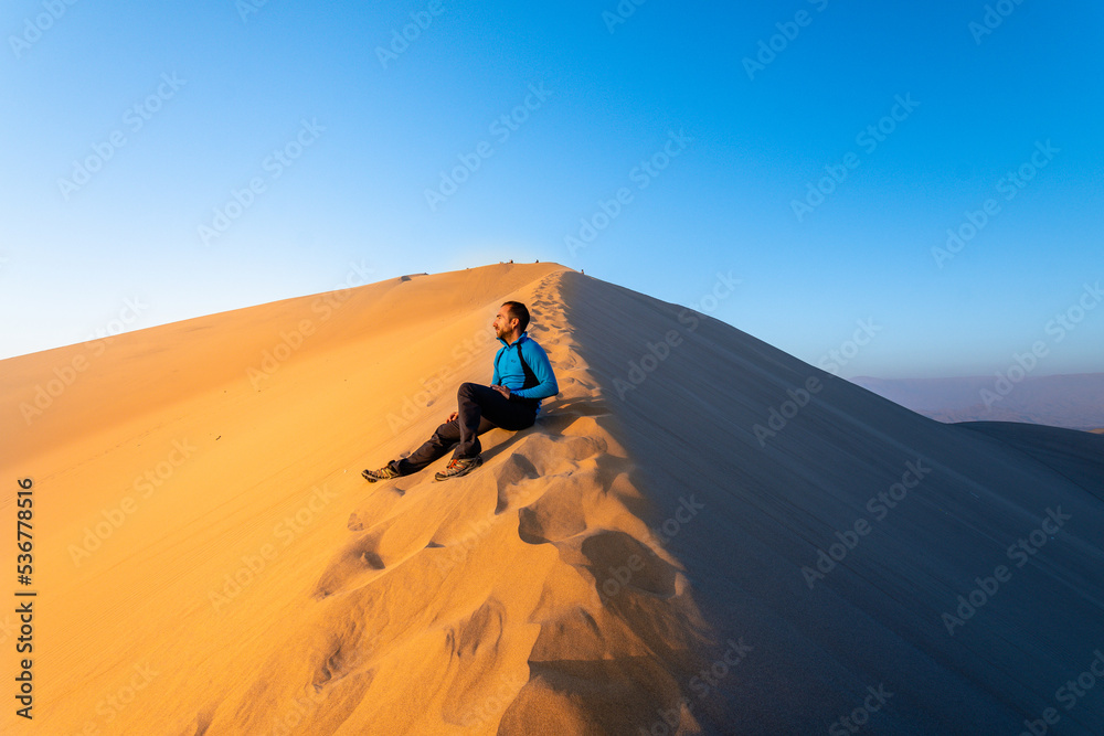 a man is walking throught sand dunes in huacachina, peru a man is walking throught sand dunes in huacachina, peru