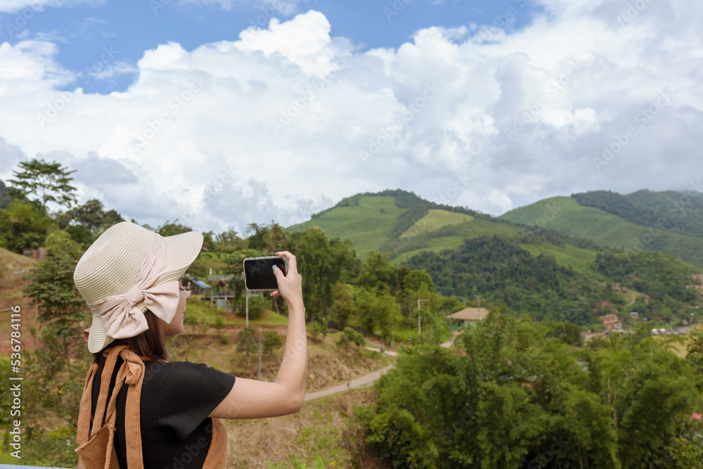 back view of woman wearing black t-shirt and hat lift smart phone up to take a photo,seeing the nature foogy over mountain,travel concept