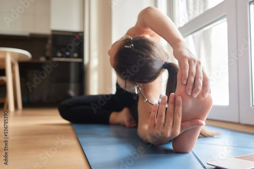 Close-up of a girl doing an asana bending forward with her hands towards her legs. Sitting on the floor on a pink yoga mat. Grip on foots. Marma points. photo