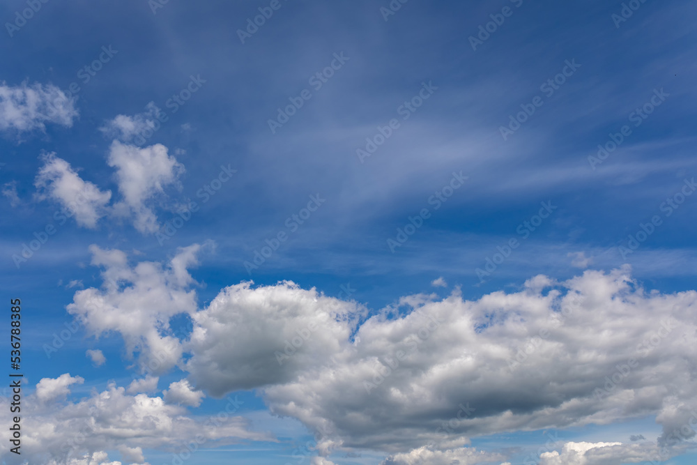 High summer sky with white cumulus clouds. Wind blows fluffy white clouds in blue sky High summer sky with white cumulus clouds. Wind blows fluffy white clouds in blue sky