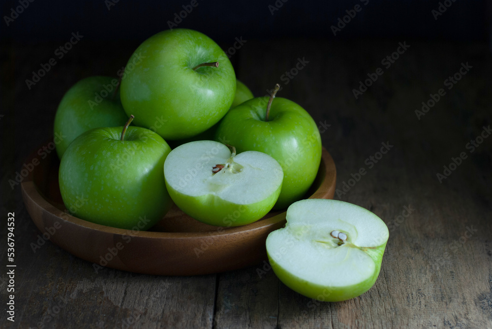 Green apples, whole, and halves are placed in a wooden tray and rest on a rustic wooden floor. Green apples, whole, and halves are placed in a wooden tray and rest on a rustic wooden floor.
