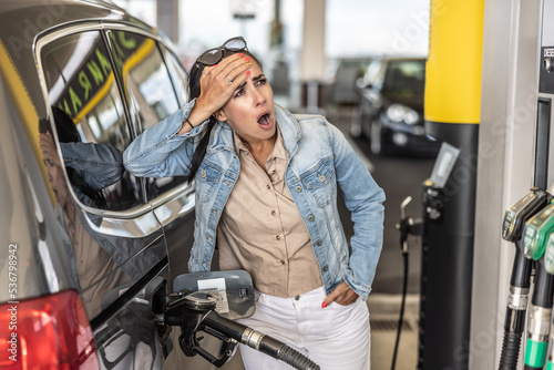 Obraz na płótnie Woman refuelling the tank of her car with diesel looks shocked with mouth open seeing the high price of fuel w salonie