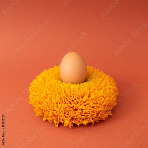 Egg in flower that looks like a nest against pastel red background. Minimal Easter idea.