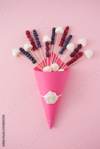Bouquet of blueberries, raspberries and marshmallows on a pastel pink background. Creative food concept. Minimal flat lay.